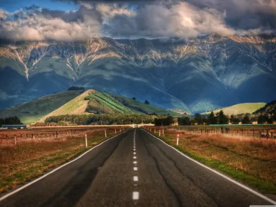 Дорога в окружении полей с видом на холмы и горы Новой Зеландии | Обои для  телефона