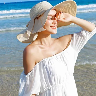 Счастливая туристка в широкополой шляпе и белом купальнике лежит на пляже