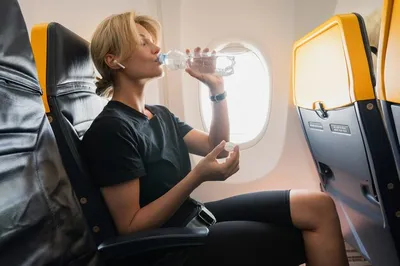 Молодая женщина пьет воду во время полета в самолете | Премиум Фото