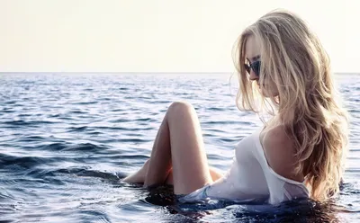 Счастливая женщина в белой рубашке сидит на пляже в брызгах волн стильная  загорелая девушка отдыхает на берегу моря и наслаждается волнами летние  каникулы внимательность и беззаботный момент | Премиум Фото