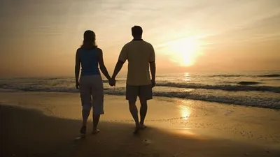 Пара гуляет на берегу моря в белых топах во время заката · Бесплатные  стоковые фото